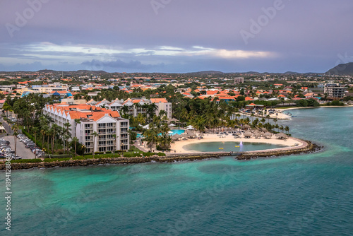 Panoramic view of Oranjestad, Aruba, showcasing colorful Dutch Caribbean architecture, palm trees, and waterfront with turquoise sea under dramatic evening sky