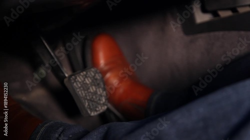 Close up view of a man's legs and feet wearing brown leather shoes and blue jeans while driving a car and pressing the brake and accelerator pedals.