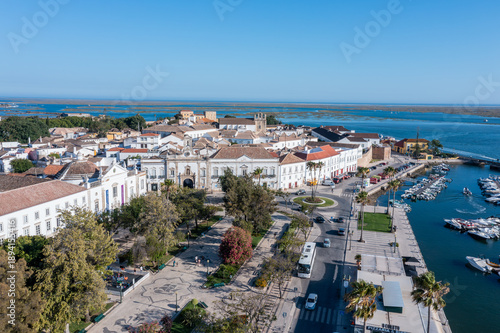 Visitors walk along the dock in the harbor of Faro while enjoying views of the historic buildings and the water of Ria Formosa in Algarve, Portugal