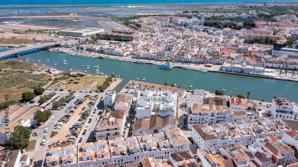 Naklejka premium Tavira in Algarve shows a Gilao river lined with boats and buildings. The scene captures the town's layout and architecture from a high viewpoint