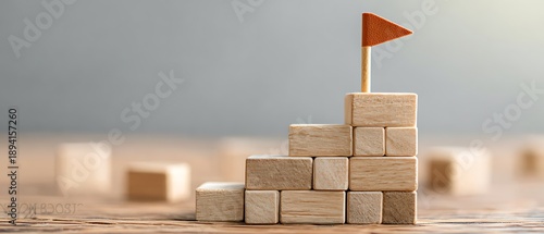 Wooden block tower with flag represents goals and success, achieved step by step. Strategy and planning are key for fulfillment.