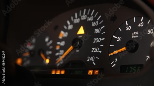 Close up view of a car dashboard instrument cluster focusing on the tachometer with the needle moving up and down as the engine revs, speedometer visible in background.

