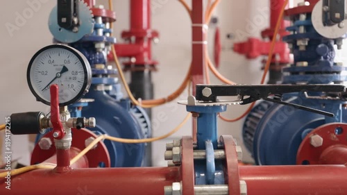 fire extinguishing system, fire suppression, fire equipment. Close-up pressure gauge and valve assembly on red and blue fire protection system inside industrial facility.