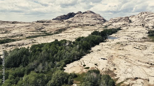 A breathtaking bird’s-eye view of a natural landscape featuring massive stone mountains cut through by a lush green valley with trees and water.