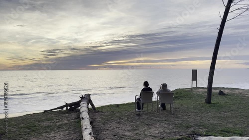 mother and daughter sitting on sandy beach on sunset on spring day. Back view. beach on Algarve coast in Portugal
