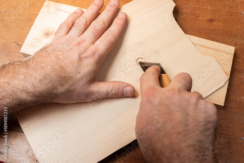 A craftsman uses a knife to cut a pattern for the deck of a talharpa