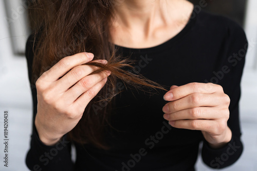 womans hands examine the ends of her long brown hair in close-up. personal care beauty routine health hair damage check concept