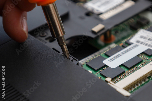 The process of disassembling or repairing a laptop using a screwdriver, showing internal microchips and case parts.