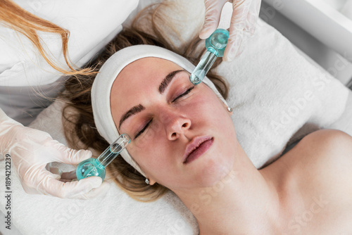 A professional aesthetician performs a cooling facial massage on a young woman using blue glass ice globes to reduce puffiness and soothe the skin during a spa skincare treatment.
