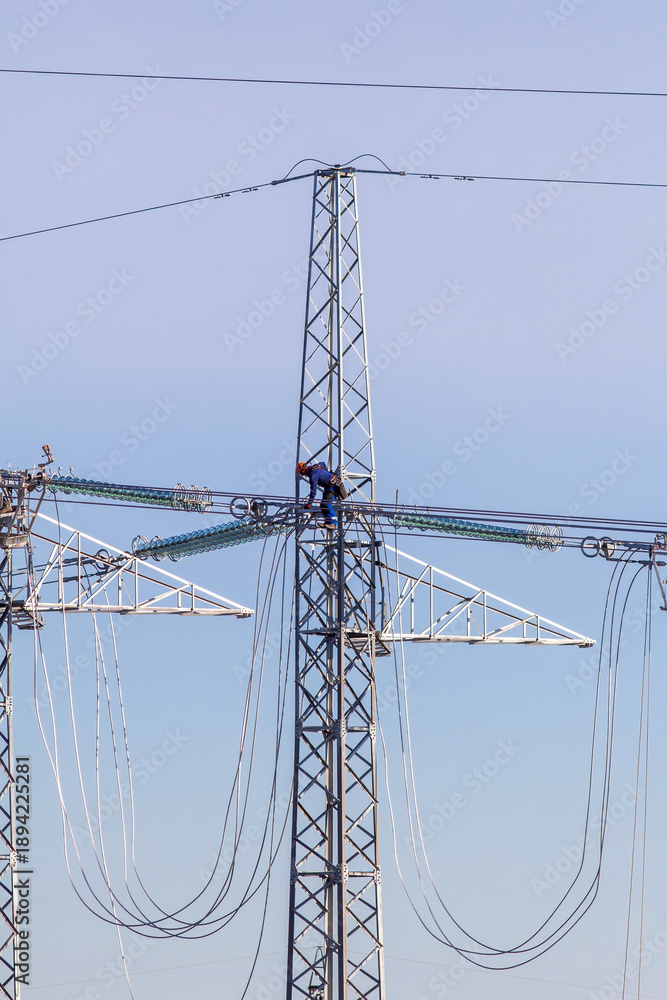 Fototapeta premium Technicians working on high voltage power lines atop transmission tower.