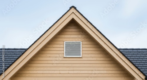 A white ventilation grille installed on the wooden gable of a modern house against a blue sky.