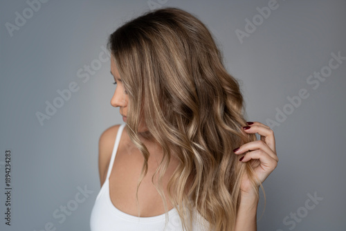 Young blonde woman showing airtouch blond hair coloring, soft wavy hairstyle, natural texture, healthy shiny hair, professional beauty styling concept
