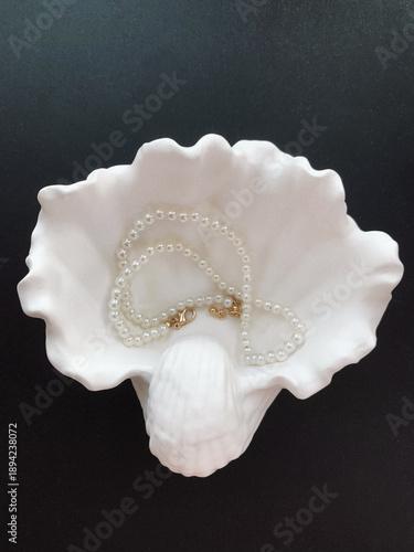 Pearl necklace and seashell on black background