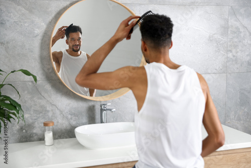 Bild auf Leinwand Handsome man combing his hair near mirror in bathroom