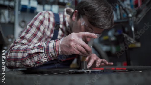 Skilled serviceman in workshop performs maintenance on mountain bike, fixing hub and bearings. Dressed in workwear, he ensures proper lubrication and repair for optimal performance and durability. 