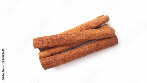 Four cinnamon sticks (Cinnamomum verum) on a white background. The sticks are cylindrical, with a rich brown hue and textured surface, characteristic of dried bark. They are neatly arranged