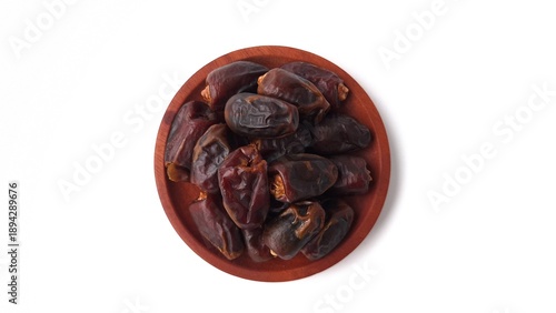 Pile of dates (Phoenix dactylifera) in a small wooden bowl. The dates appear dark brown and glossy, showcasing their natural wrinkled texture. The wooden bowl has a smooth, polished finish