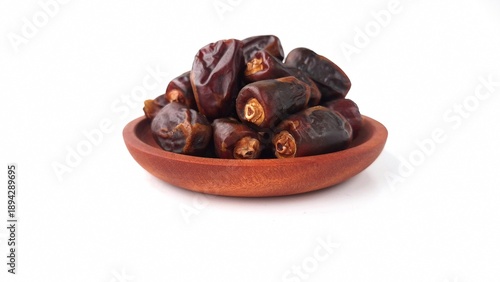 Pile of dates (Phoenix dactylifera) in a small wooden bowl. The dates appear dark brown and glossy, showcasing their natural wrinkled texture. The wooden bowl has a smooth, polished finish