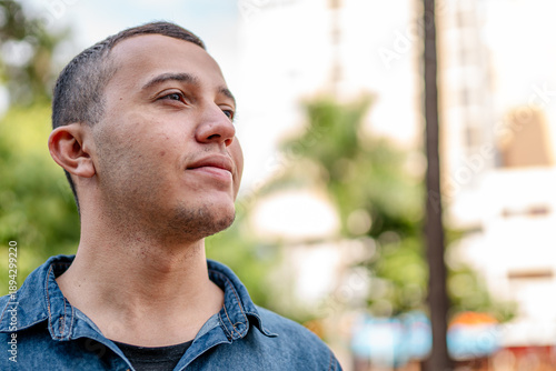Fotografi Thoughtful young man in a denim shirt looking into the distance outdoors in a ci