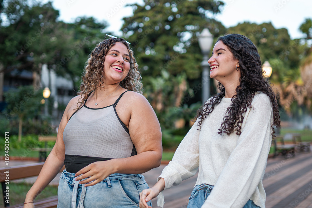 Fototapeta premium Two happy young female friends walking and laughing together in a city park