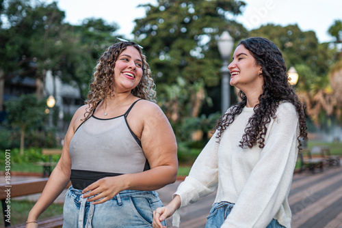 Cuadro en lienzo Two happy young female friends walking and laughing together in a city park