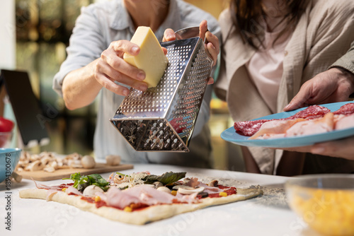 Foto Fun times at the kitchen counter as family is grating cheese and mozzarella on pizza dough, preparing homemade pizza together