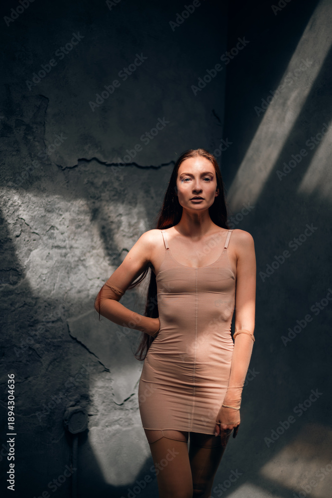 Fototapeta premium Woman stands in a bare room with one arm raised while light streams through ceiling windows during day time