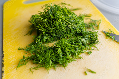 Chopping dill on yellow cutting board with knife