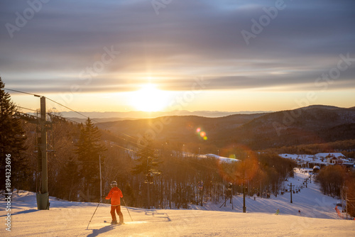 A chairlift at a ski area in Bolton Valley, Vermont at dusk with a nice sunset behind. Night skiing down a snowy winter slope adventure.