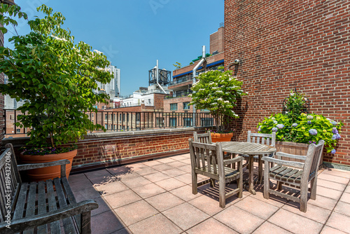 Canvas Print Urban rooftop terrace with wooden table and chairs surrounded by brick buildings