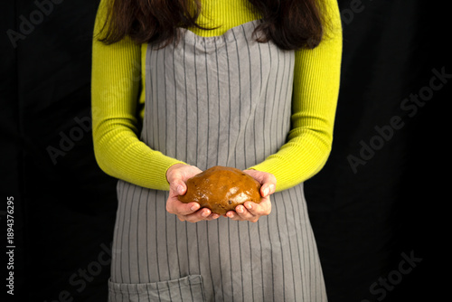 Wallpaper Mural Woman in apron holding raw cookie dough in hands, ready for baking preparation. Close-up of homemade dessert making in kitchen with dark background Torontodigital.ca