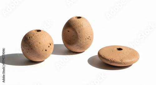 Three rustic, handmade terracotta-like objects with central holes, casting shadows on a white surface.
