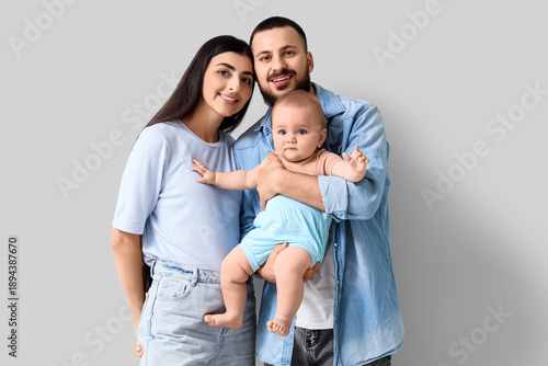 Happy young family and cute little baby on grey background