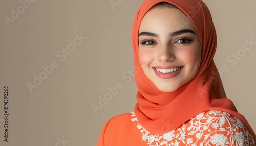 Radiant young woman wearing a bright orange headscarf smiles sincerely against a muted background
