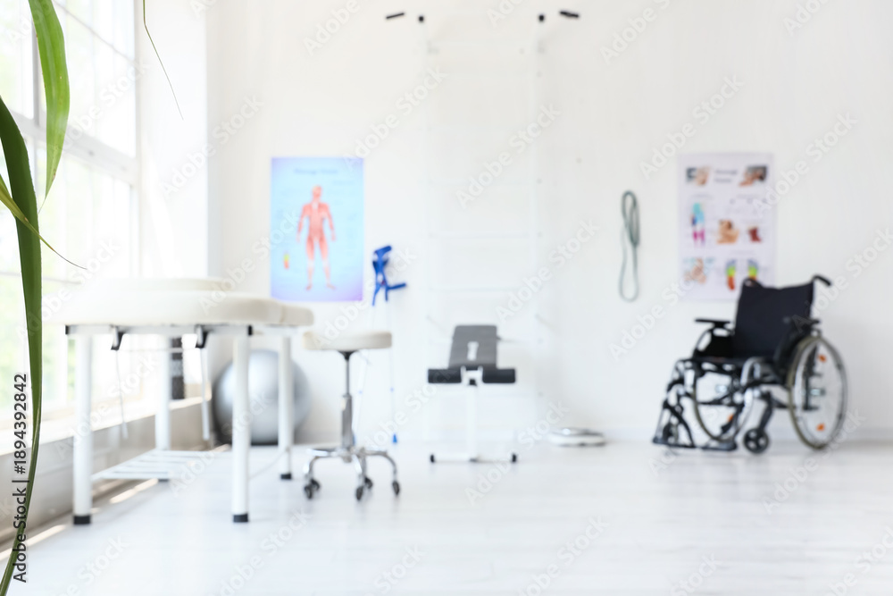 Fototapeta premium Blurred view of physiotherapist's office with couch, sports equipment and wheelchair