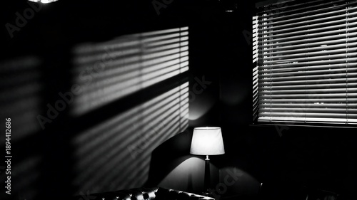 Dramatic light and shadow play from venetian blinds illuminating a table lamp in a dark room