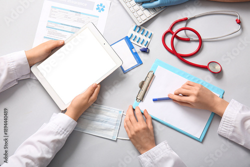 Doctor's hands with tablet and clipboard near stethoscope on white background