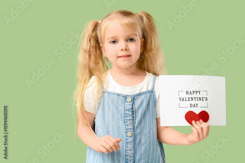 Cute little girl holding greeting card with text HAPPY VALENTINE'S DAY and heart on green background