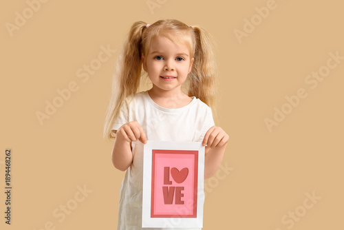 Cute little girl holding greeting card with word LOVE and heart on beige background. Valentine's Day celebration