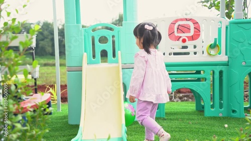 Adorable toddler girl sliding down play equipment in a colorful outdoor playground, enjoying a sunny day with vibrant toys and greenery around her