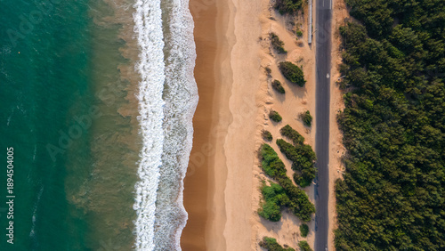 High-angle aerial view of the Puri Konark Marine Drive coastline in Odisha, India, featuring golden sand beach, crashing waves, and lush greenery by the sea