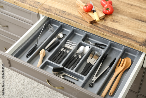 Open kitchen drawer with different silver cutlery and fresh tomatoes on board © Pixel-Shot