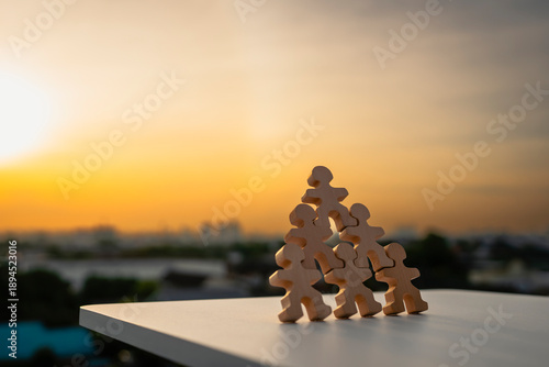 Canvas Print Wooden human figures stacked like pyramid on unstable surface at sunset symbolizing structural weakness, domino effect, system failure, leadership risk, collapse of organization, and instability