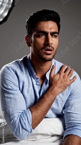 A man in a blue shirt is grimacing while holding his shoulder, showing discomfort