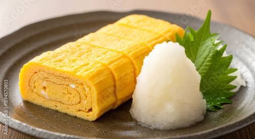 Traditional Japanese tamagoyaki served with grated daikon radish and shiso leaf on a ceramic plate, showcasing classic Japanese presentation.