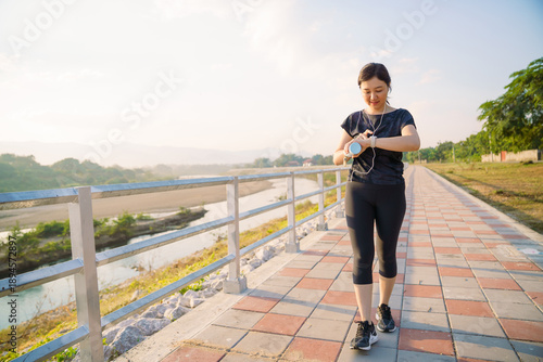 Asian woman checking smartwatch while walking outdoors. Virtual fitness assistant technology.