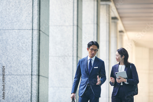 会話をしながら屋外を歩くビジネスマンとビジネスウーマン
