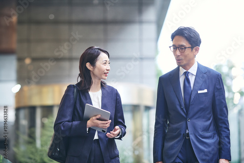 会話をしながら屋外を歩くビジネスマンとビジネスウーマン