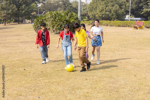 Group of indian children playing soccer or foot ball in summer park, Playful asian kids enjoying fun outdoor sports activity. friendship and togetherness. Childhood.