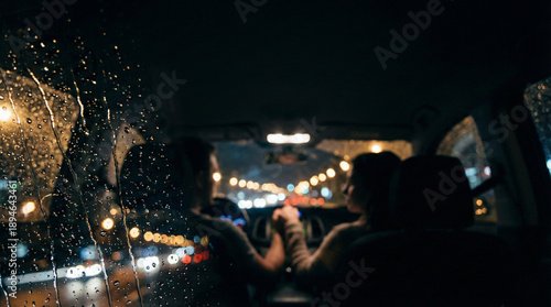Couple sitting in a car at night, watching city lights through the windshield. Raindrops on the glass in sharp focus,